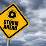 Photo of cloudy sky with a yellow sign that reads "Storm Ahead".